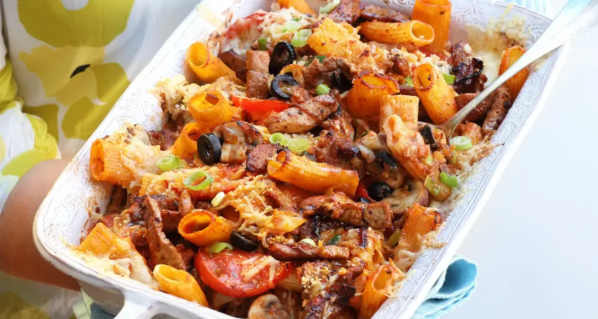 Pyszna zapiekanka gyros z makaronem, podana w białym naczyniu, z widocznymi kawałkami mięsa, oliwek i pomidorów.