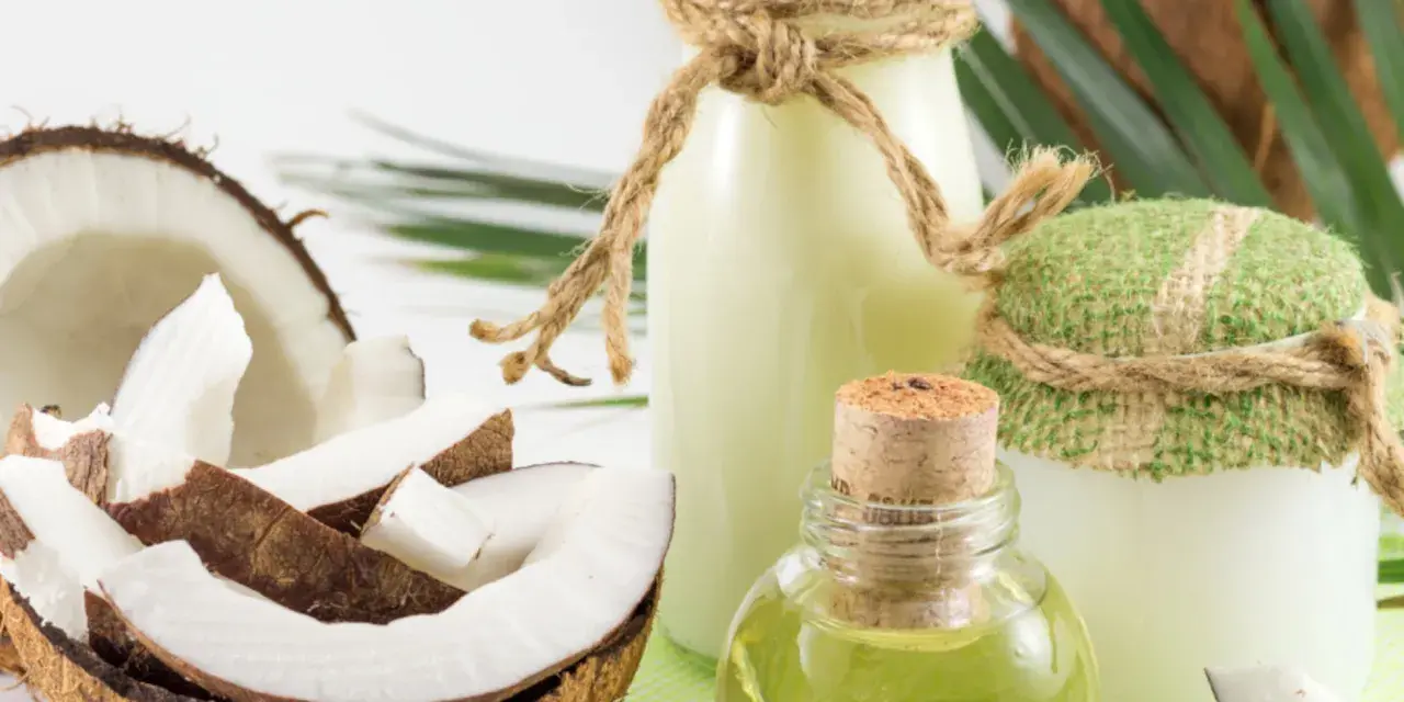 Aceite de coco para el pelo en frascos y botellas, junto a cocos frescos y hojas verdes.