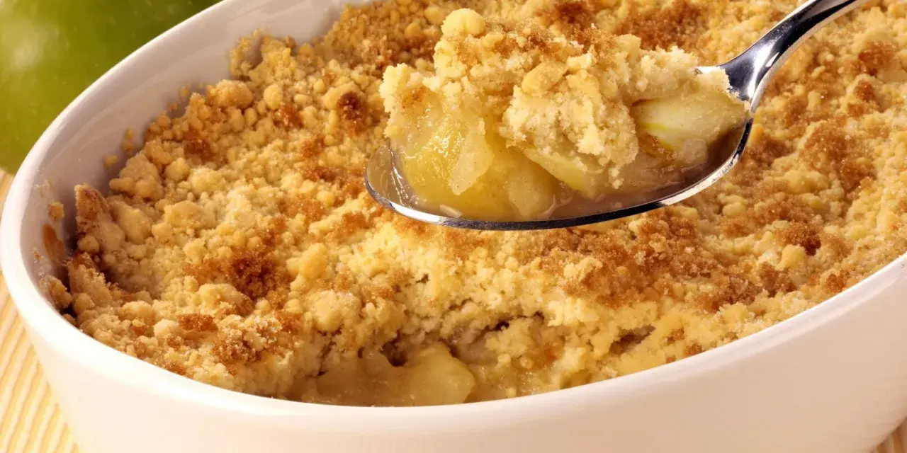 Une cuillère de crumble aux pommes, parfait pour suivre la recette Cyril Lignac. Des pommes fondantes sous une pâte croustillante.