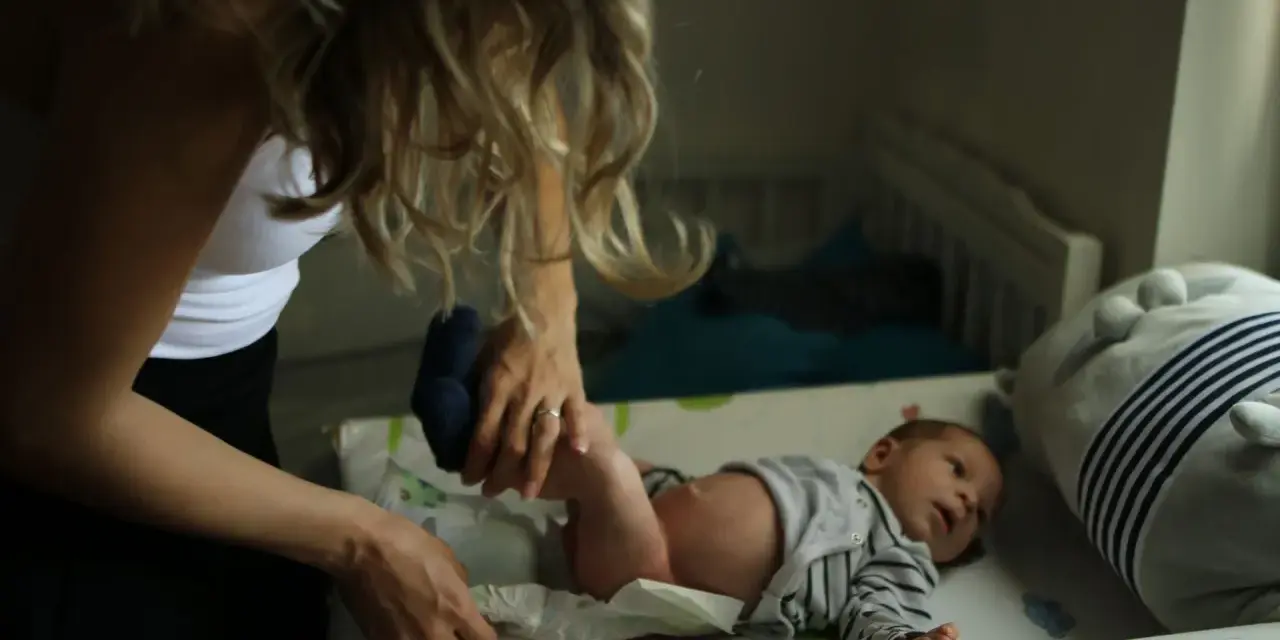 Mama zmienia pieluszkę noworodkowi. Zastanawiasz się, ile kupić pieluszek dla noworodka? Warto mieć zapas!