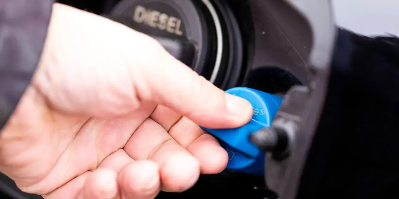 Hand schraubt blauen AdBlue-Deckel auf Diesel-Tanköffnung. AdBlue ist eine Harnstofflösung zur Abgasreinigung bei Dieselfahrzeugen.