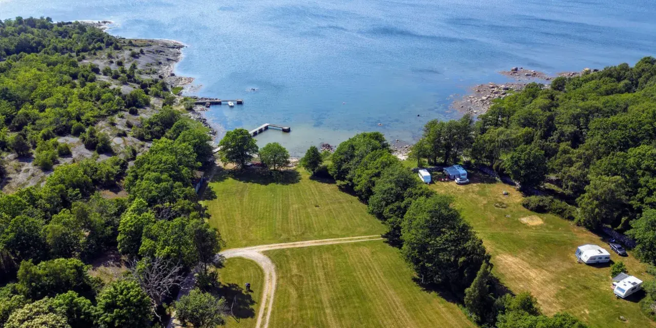 Vacker vy över camping i Blekinge med husvagnar vid en brygga och grönskande skog.