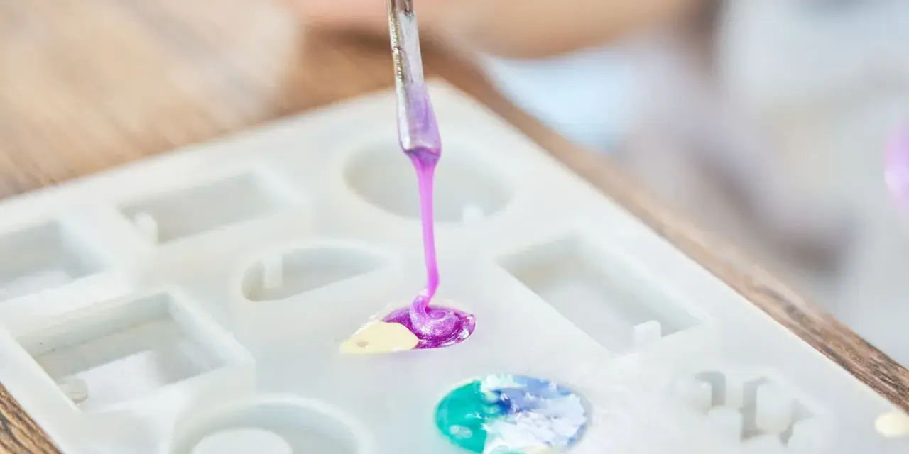 A person is learning how to make an epoxy resin mold by carefully pouring colored resin into a silicone mold.