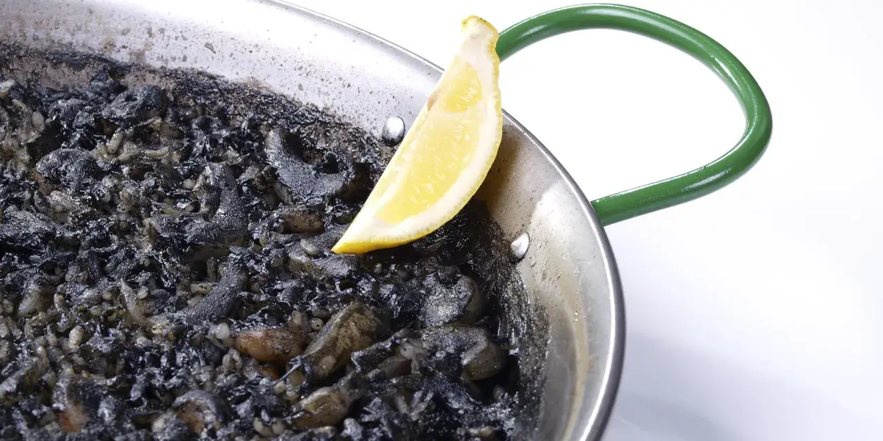 Arroz negro en paellera, con trozos de calamar y un gajo de limón.