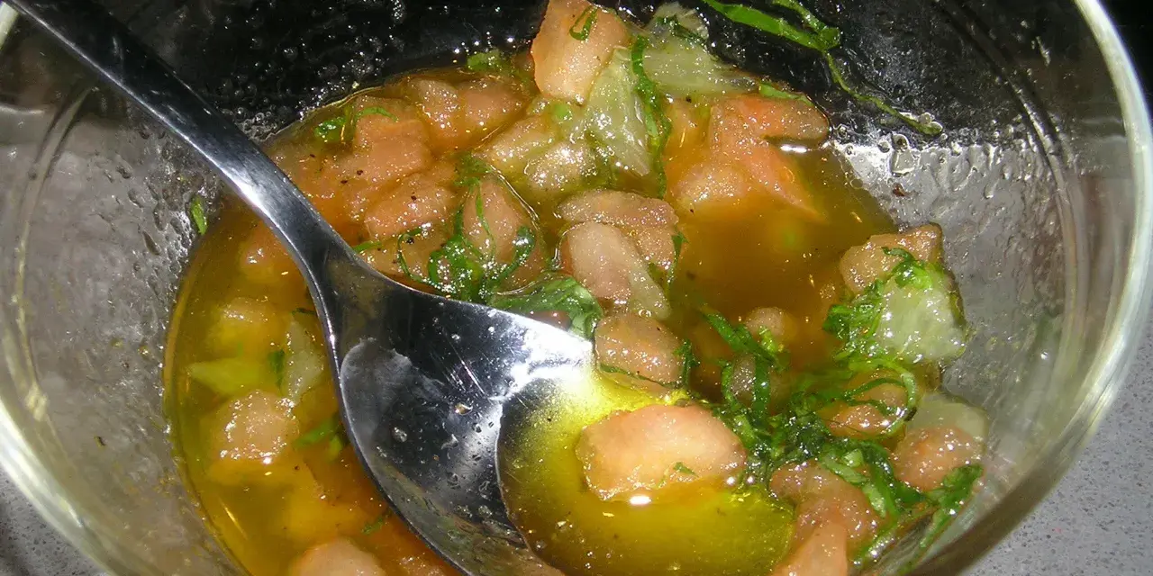Un bol de sauce vierge recette, avec des morceaux de tomates, des herbes fraîches et une cuillère en argent.