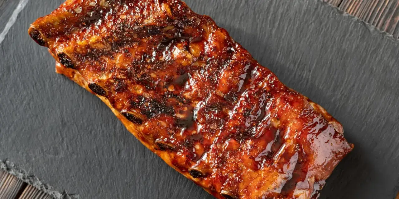 Costillas a la miel, glaseadas y jugosas, servidas sobre una pizarra oscura.