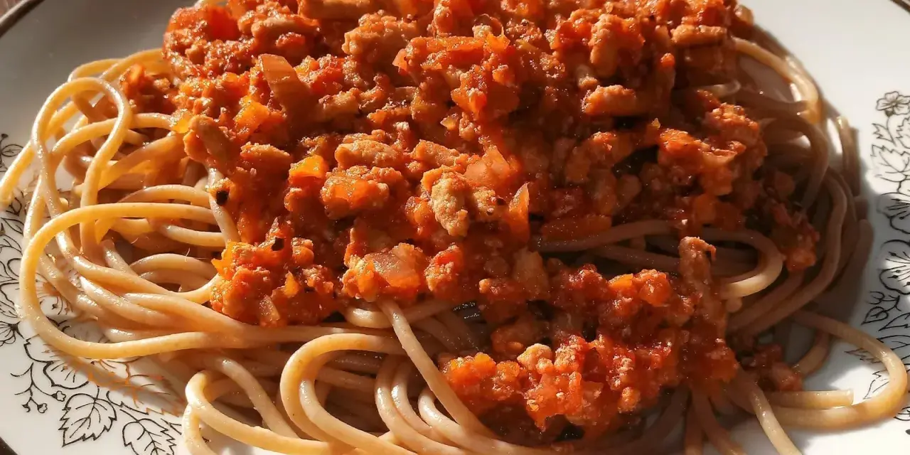 Porcja pysznego spaghetti bolognese z aromatycznym sosem mięsnym i pomidorowym, podana na talerzu z ozdobnym wzorem.