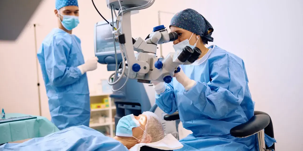 Chirurghi in sala operatoria, uno esegue una vitrectomia non riuscita con un microscopio, mentre un altro assiste.