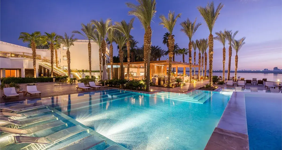 Luxury resort pool with palm trees and lounge chairs at dusk.