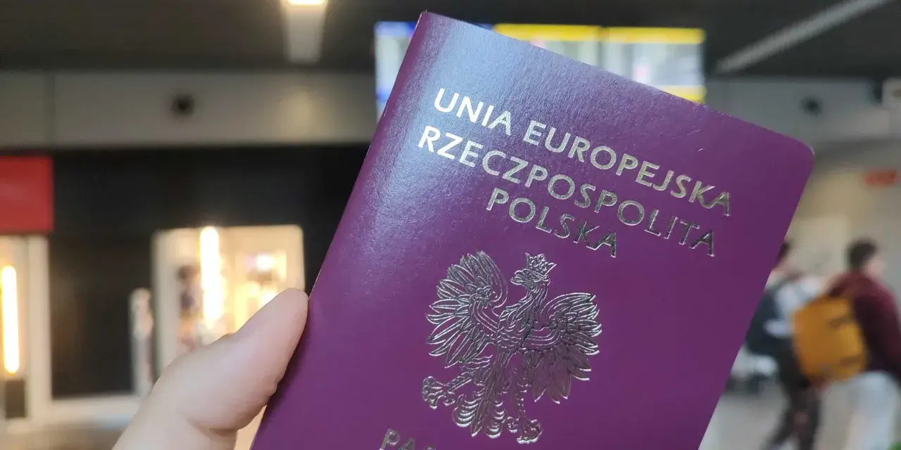 Dłoń trzyma fioletowy paszport Rzeczypospolitej Polskiej z godłem orła.