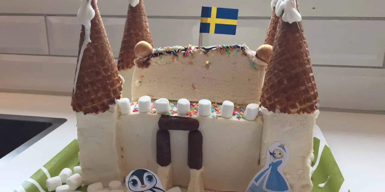 En fantasifull glasstårta slott med svenska flaggan, marshmallows och en söt pingvin.
