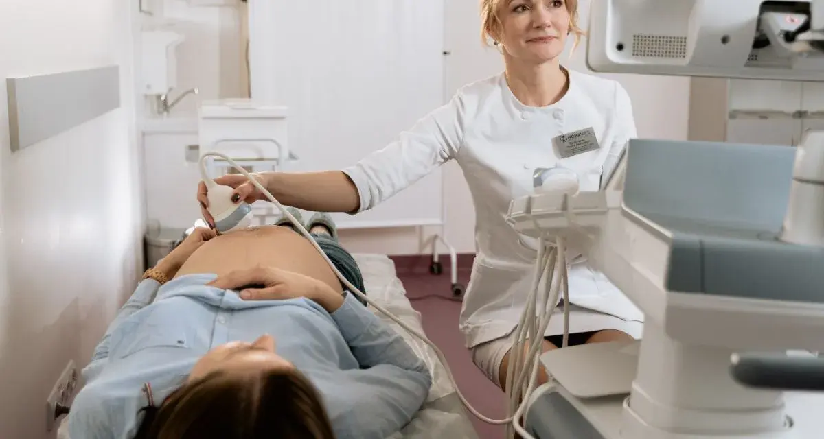 Lekarka wykonuje badania prenatalne, pokazując przyszłej mamie, jak się przygotować do wizyty.
