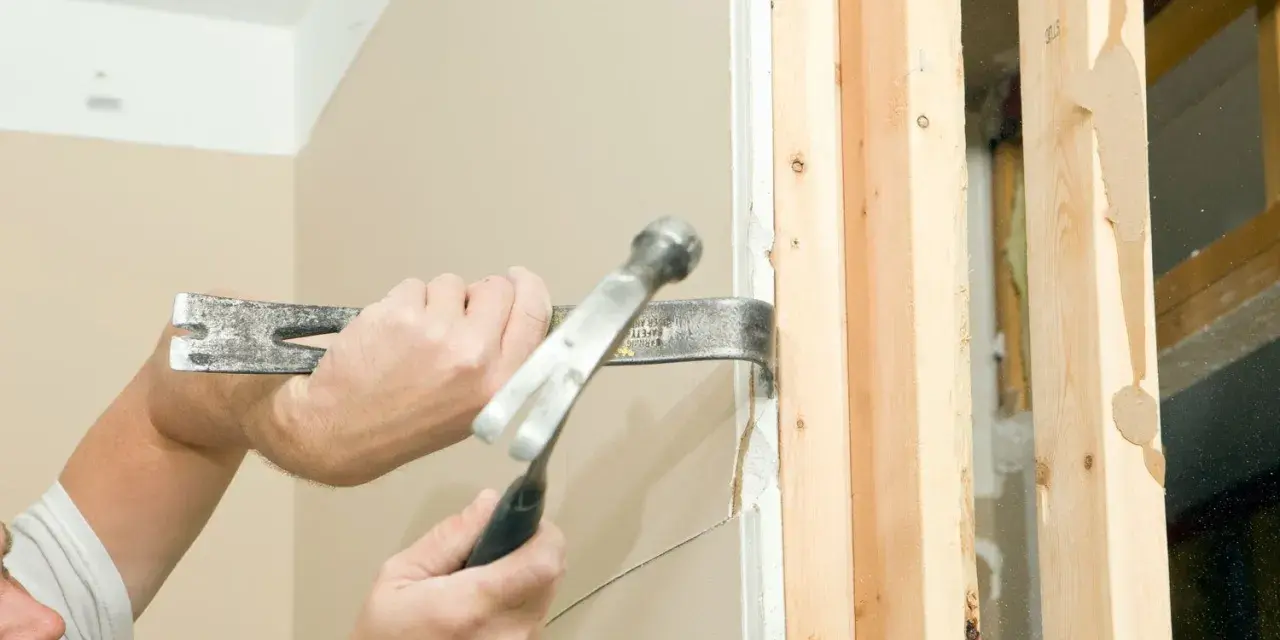 Main tenant utilise un pied-de-biche et un marteau pour démonter une cloison placo. Le travail progresse bien.
