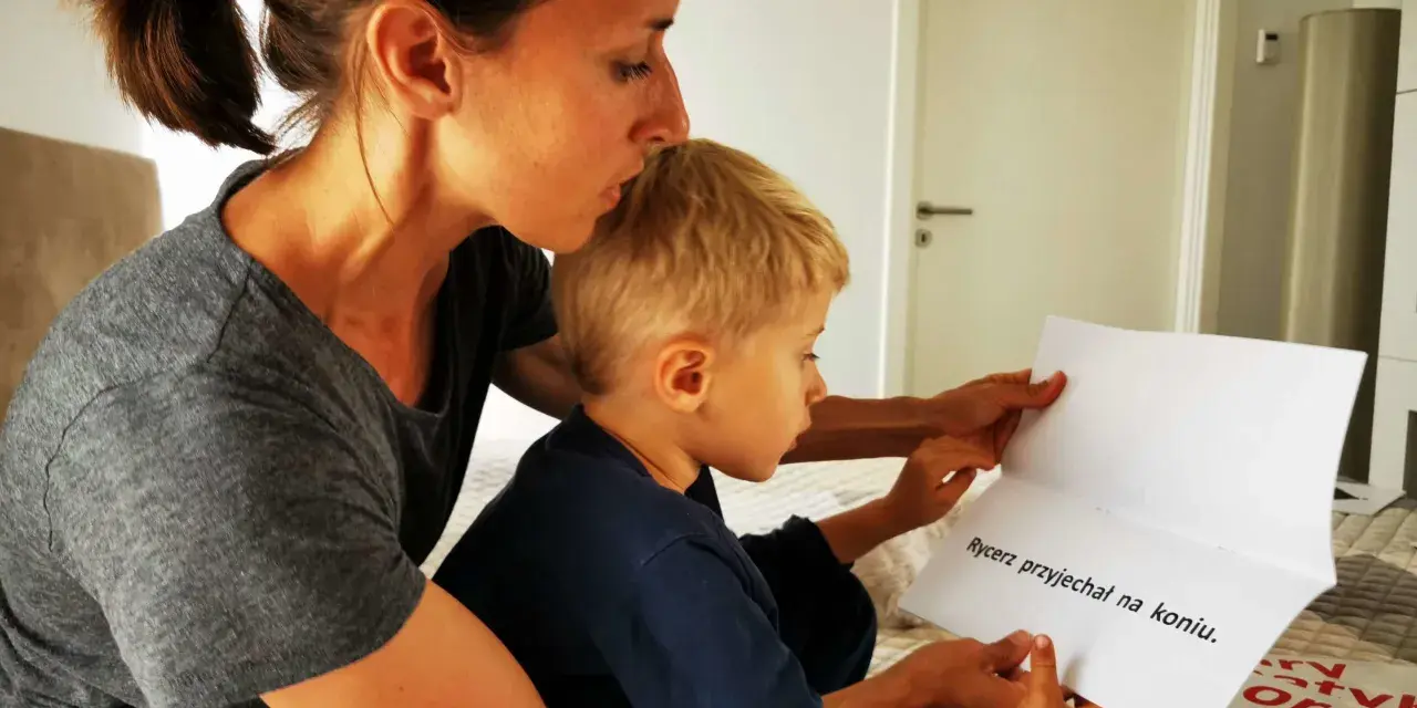 Mama pomaga synkowi, jak nauczyć się czytać, wskazując palcem na tekst "Rycerz przyjechał na koniu".