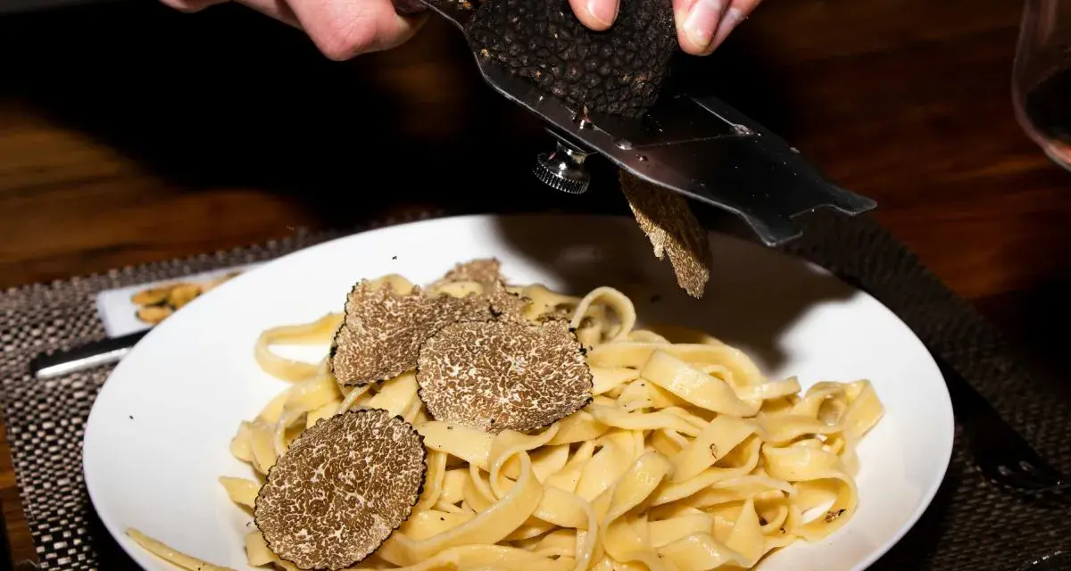 Dłonie trą całe grzyby trufle nad talerzem tagliatelle.