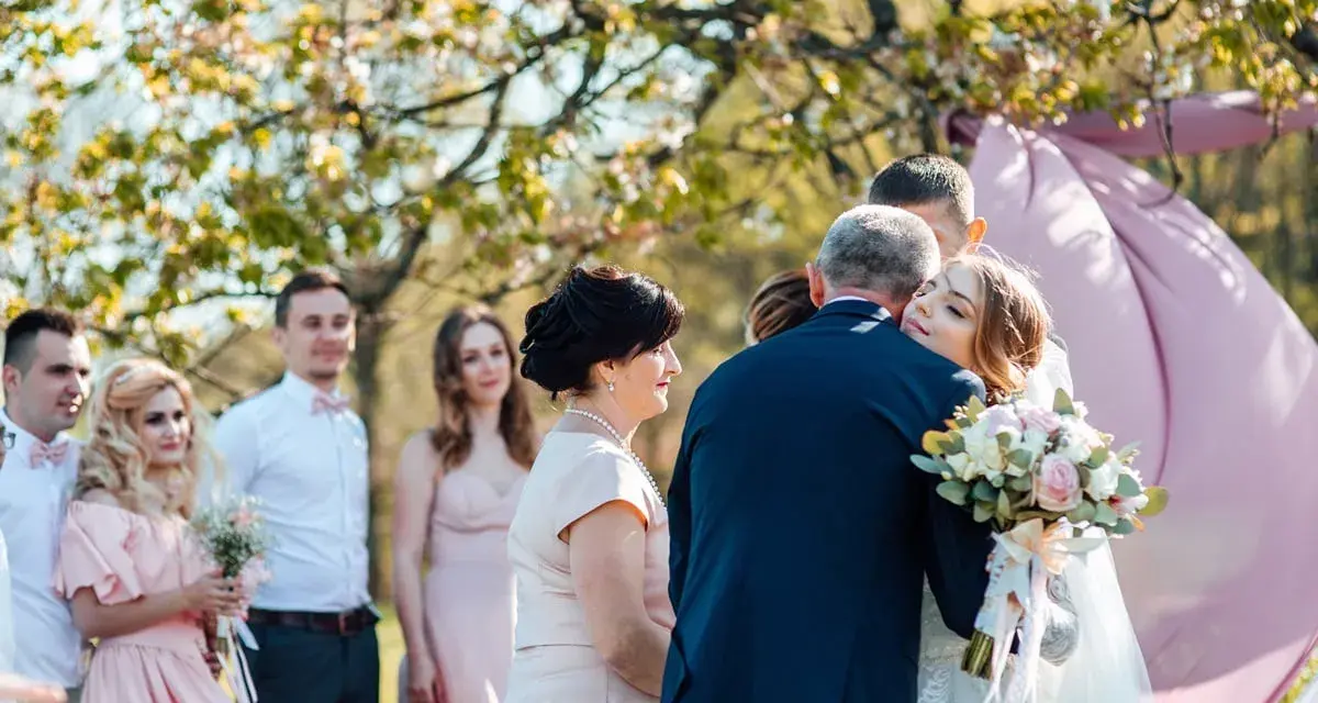 Wzruszające życzenia dla młodej pary. Panna młoda tuli się do ojca, a goście patrzą z uśmiechem.