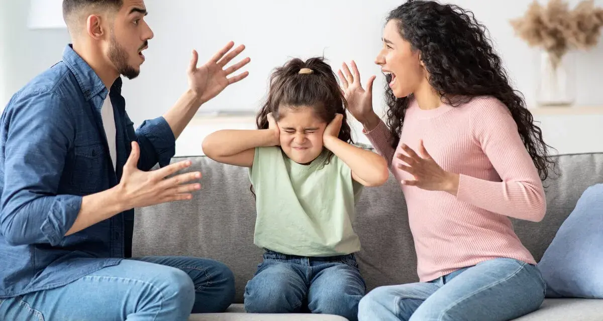Ein Kind hält sich die Ohren zu, während die Eltern streiten. Eine Szene, die zeigt, wie schwierig es ist, wenn Eltern sich trennen.