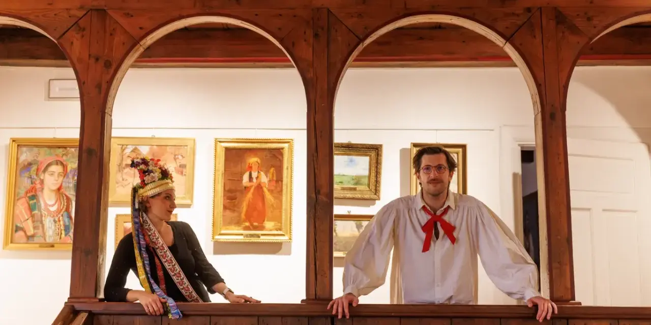 Para młoda w strojach ludowych, jak z polskiego teatru, pozuje na tle obrazów.