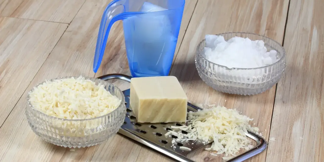 Ingrédients pour une lessive maison : savon râpé, cristaux de soude et un bloc de savon sur une râpe.