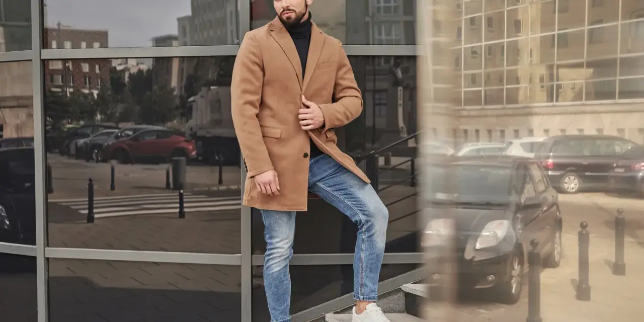Mężczyzna w czarnym golfie i beżowym płaszczu stoi na schodach.