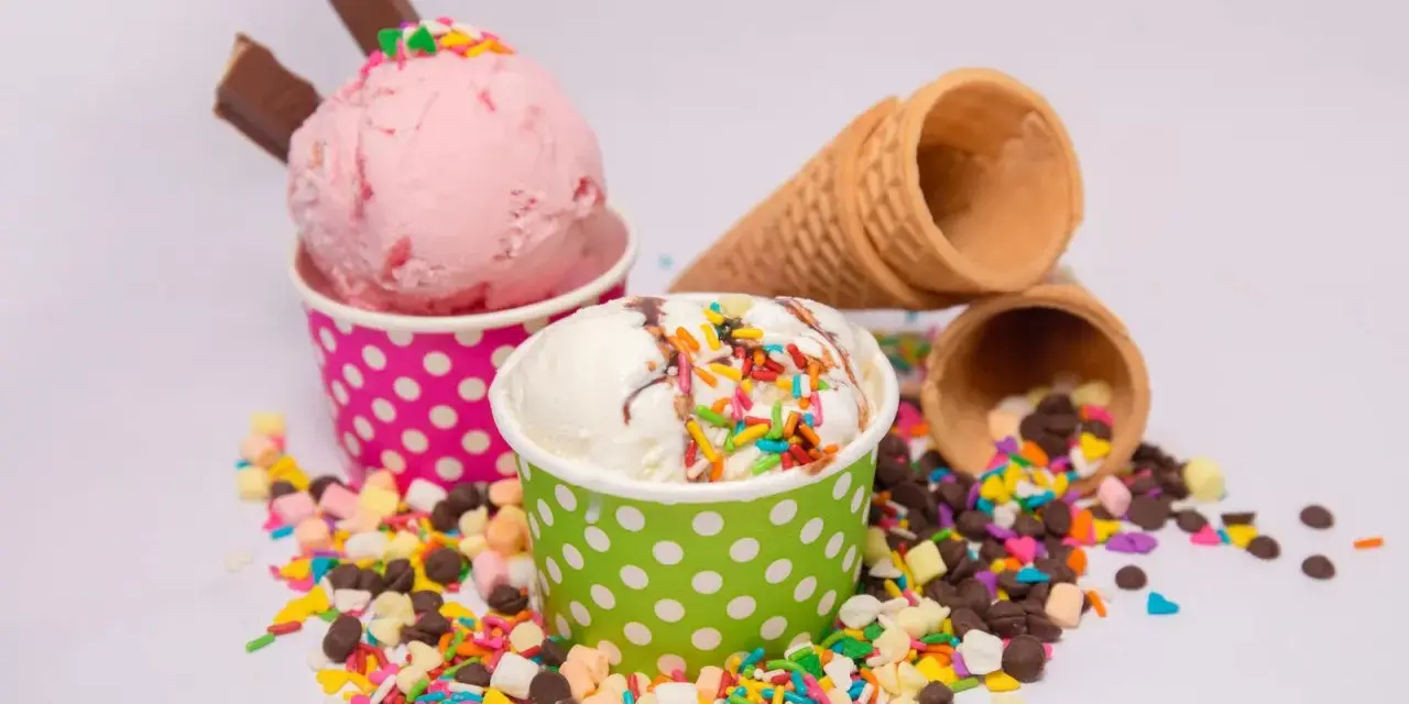 Zwei Becher mit Eiscreme, einer rosa, der andere weiß, bestreut mit bunten Streuseln und Schokostückchen. So sieht leckeres Gelato aus!