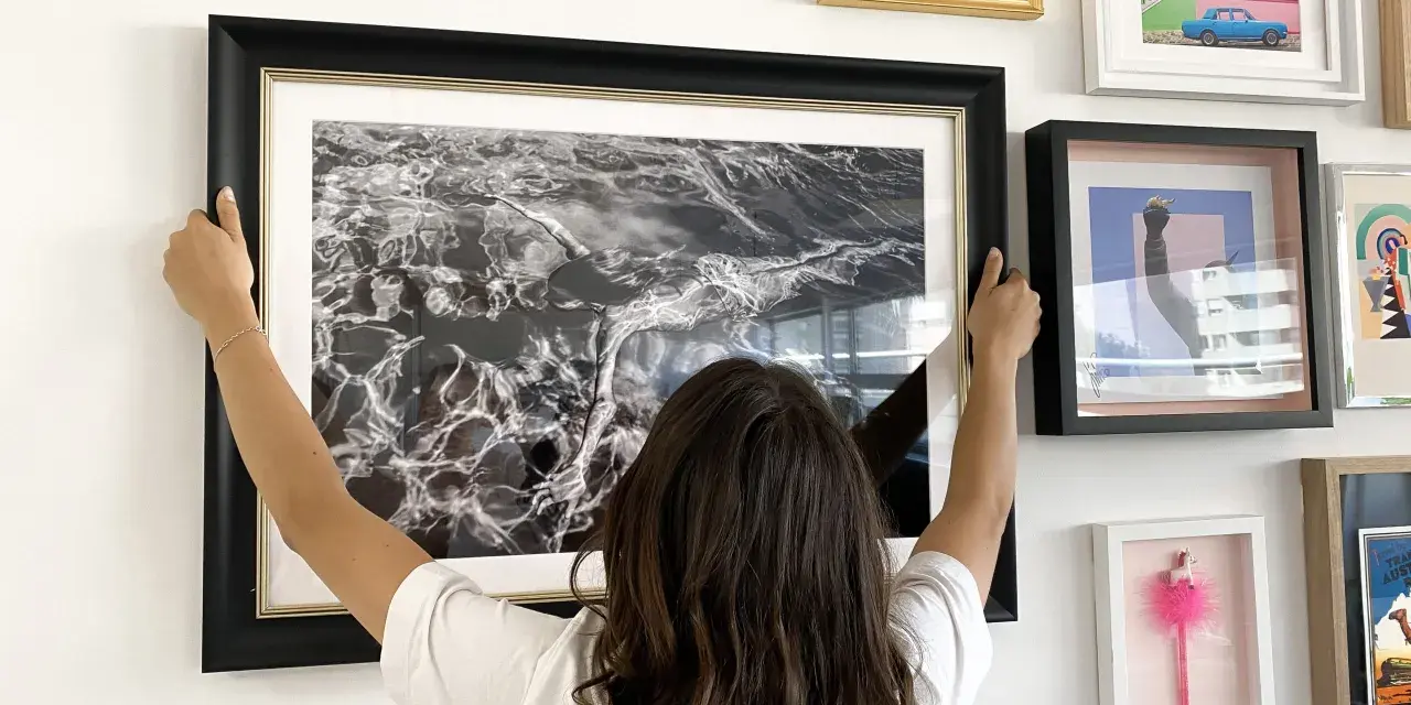 Une femme ajuste un grand cadre noir avec une photo d'eau en noir et blanc. Elle est en train de fabriquer un cadre pour sa maison.