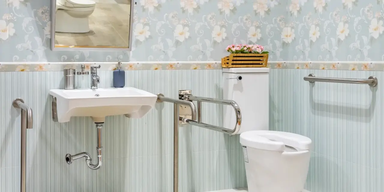 Salle de bain senior : lavabo suspendu, WC avec barre d'appui rabattable et barre d'appui murale pour plus de sécurité.