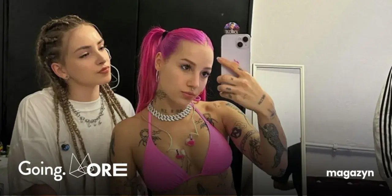 Dwie dziewczyny, jedna z różowymi włosami, druga z warkoczami, pozują do selfie. Jedna z nich, w różowym bikini, ma widoczne tatuaże. W tle logo "Going. MORE".