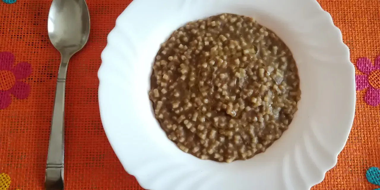 Piatto di pasta e lenticchie fumante, pronto per essere gustato. Un cucchiaio d'argento attende accanto.