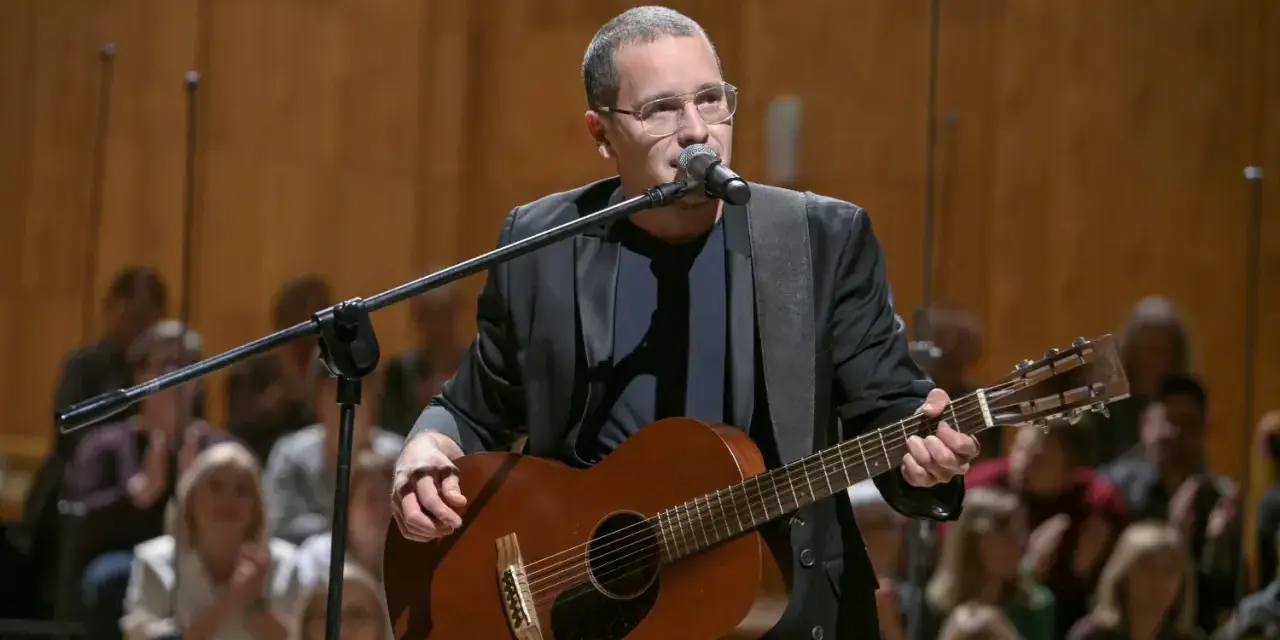 Artysta w okularach gra na gitarze podczas koncertu Męskie Granie. Publiczność w tle.