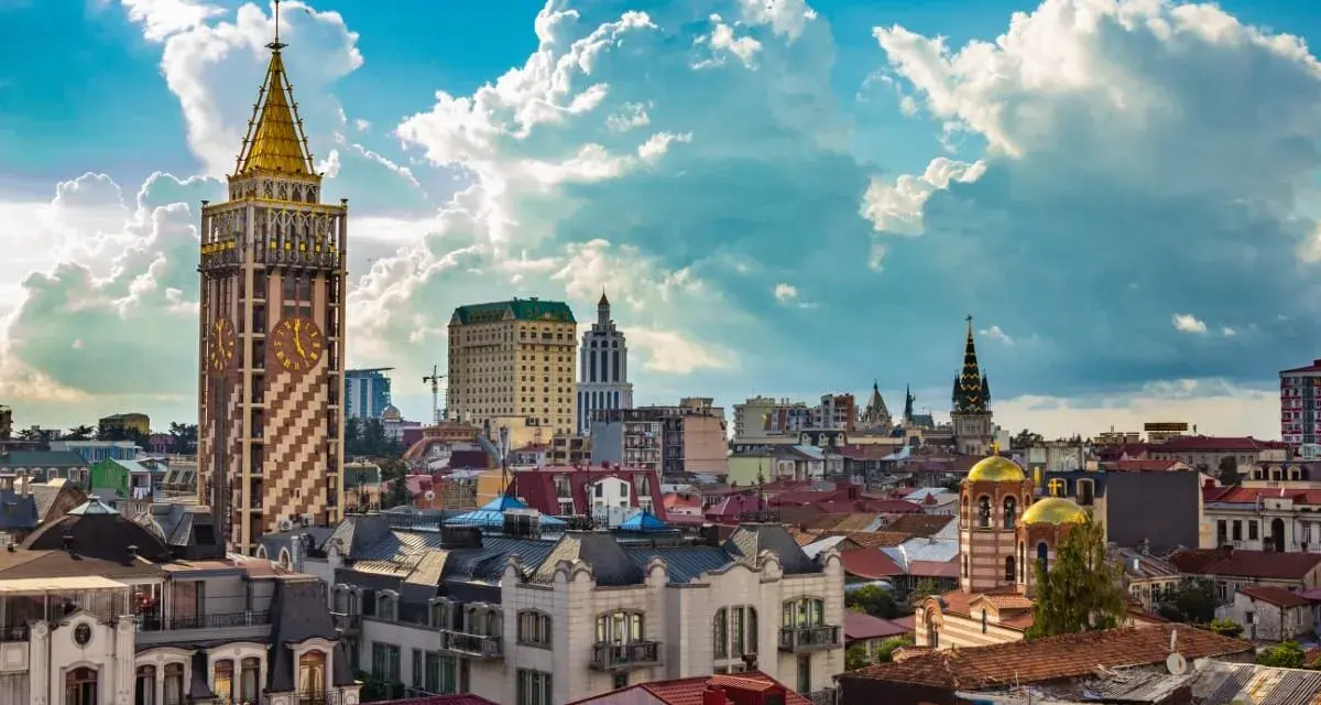 Widok na stolicę Adżarii, Batumi, z charakterystyczną wieżą zegarową i złotymi kopułami cerkwi pod błękitnym, chmurowym niebem.