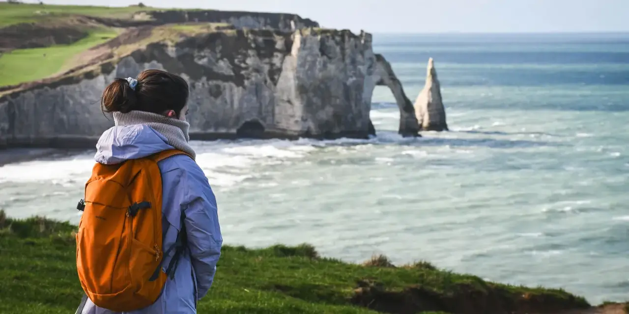 Une randonneuse admire les falaises d'Étretat, un paysage spectaculaire rappelant la beauté sauvage de la baie de Somme.