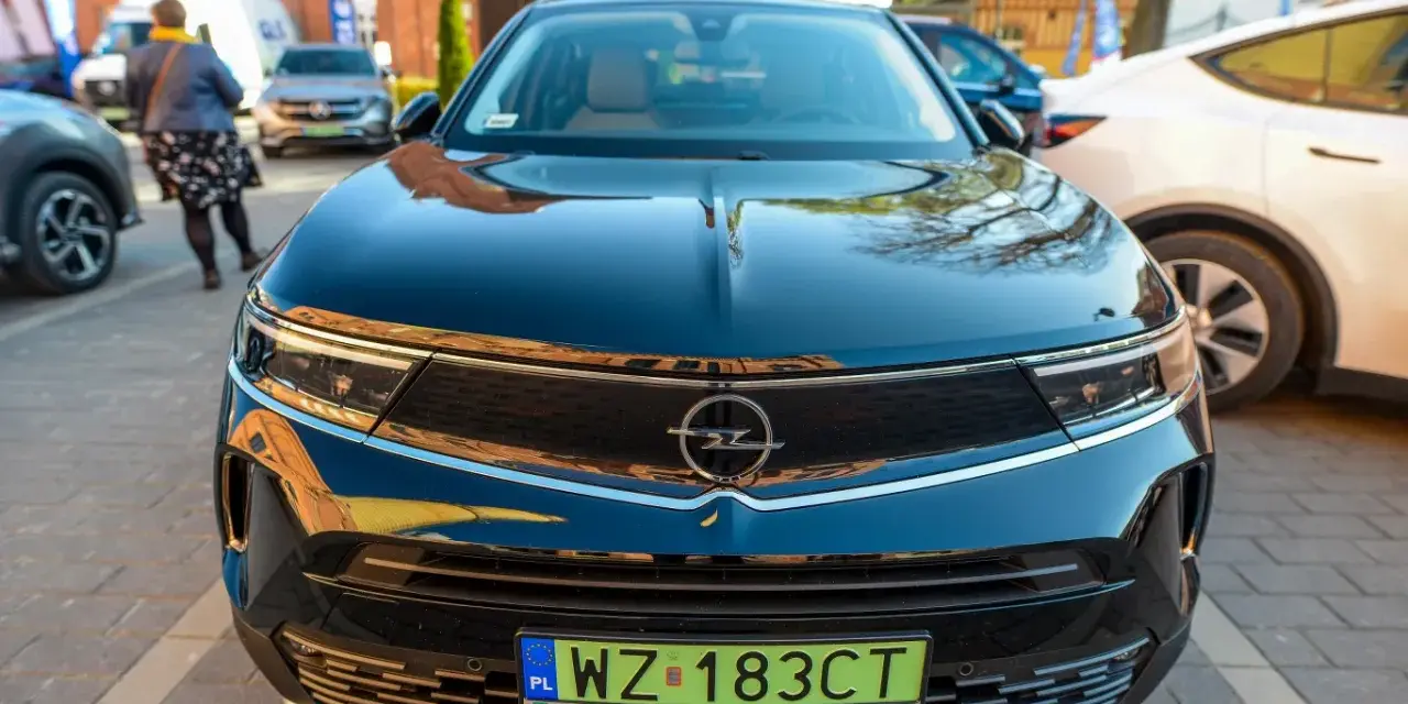 Czarny Opel z zieloną tablicą rejestracyjną WZ 183CT na tle innych samochodów.