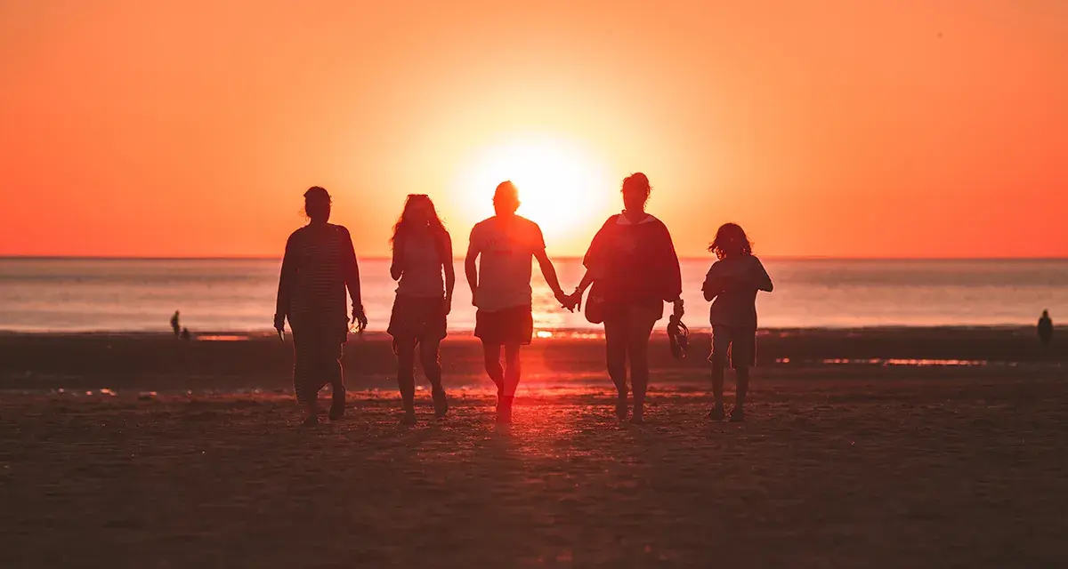 Une famille profite de ses vacances à l'étranger, marchant main dans la main sur une plage au coucher du soleil.
