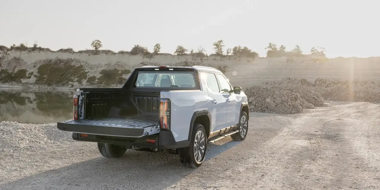 Biały maxus pickup z otwartą paką stoi na żwirowej drodze przy zbiorniku wodnym.