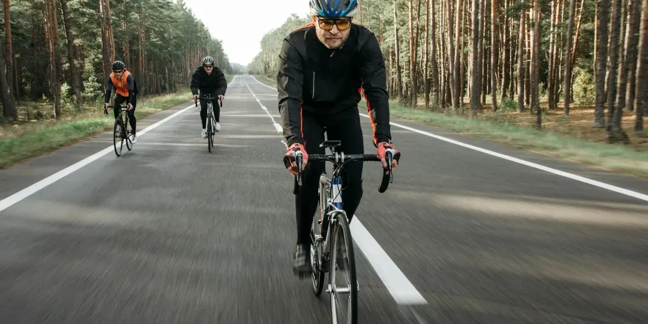 Cyclists on a road through a forest, likely engaged in a VO2 max training program, pushing their limits.
