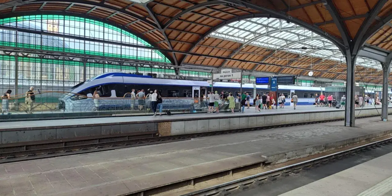 Nowoczesny pociąg kraków wrocław na peronie, pasażerowie czekają na podróż pod zabytkowym zadaszeniem dworca.