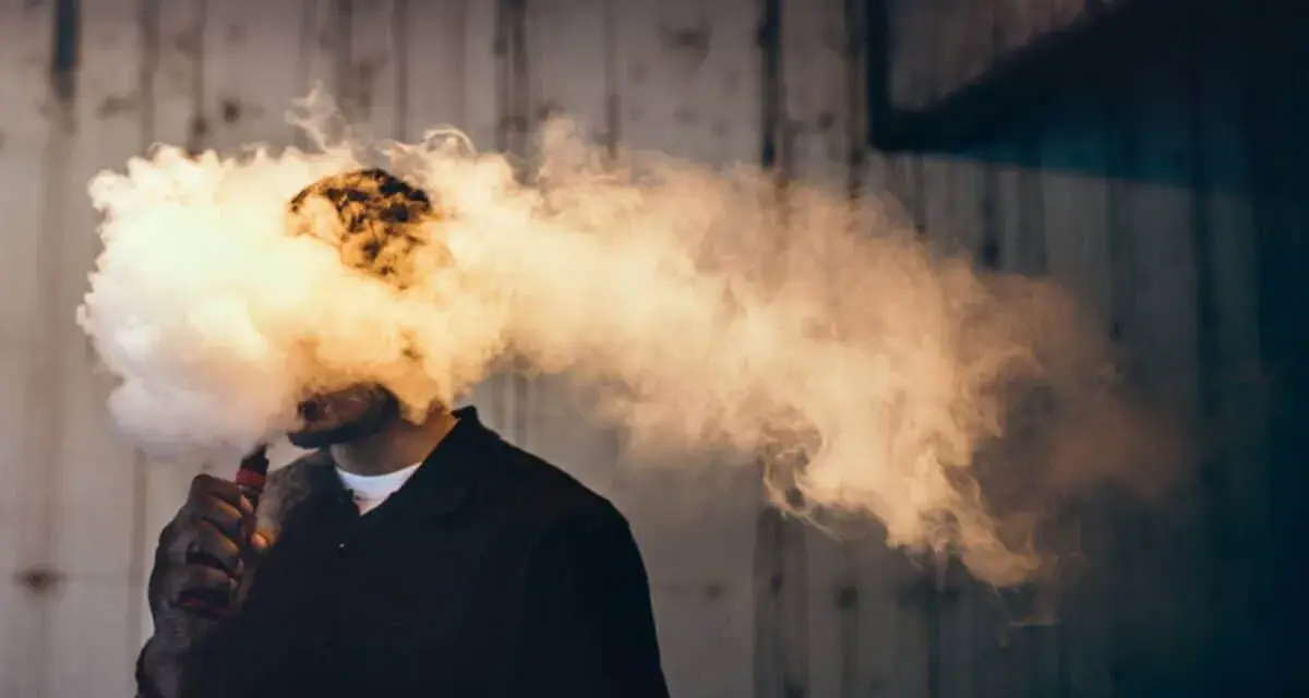 Hombre exhalando una gran nube de humo vaper, que envuelve su cabeza.