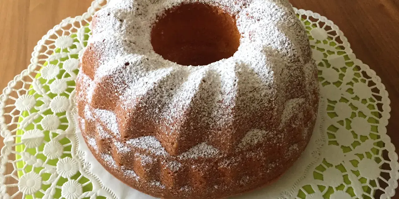 Ein goldbrauner Quark Gugelhupf, bestäubt mit Puderzucker, auf einer zarten Spitzendeckchen.