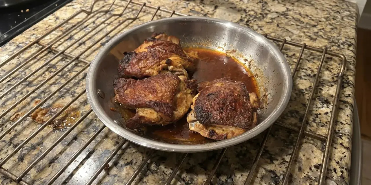 Succulente cosce di pollo in padella, dorate e saporite, riposano su una griglia.