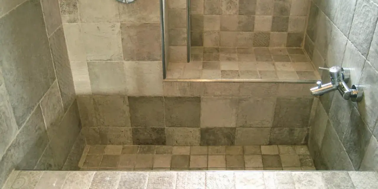 Bagno con vasca da bagno in muratura fai da te, rivestita con piastrelle grigie di varie tonalità e fantasie.