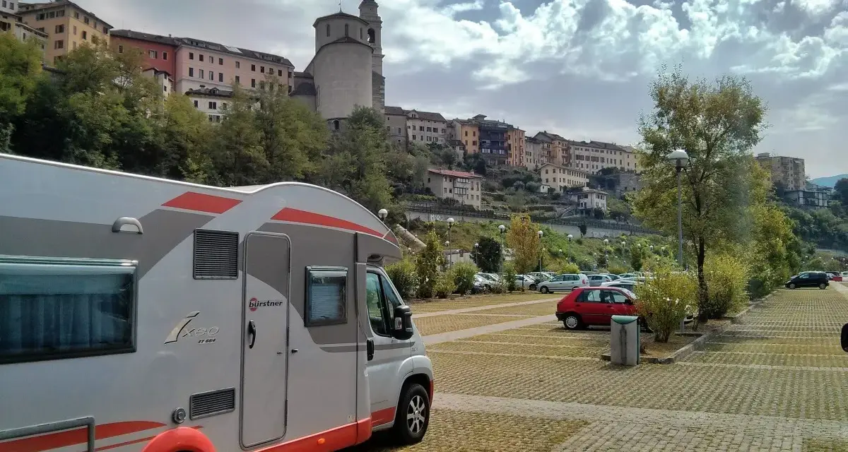 Camper in sosta a Belluno, con case colorate e un campanile sullo sfondo.