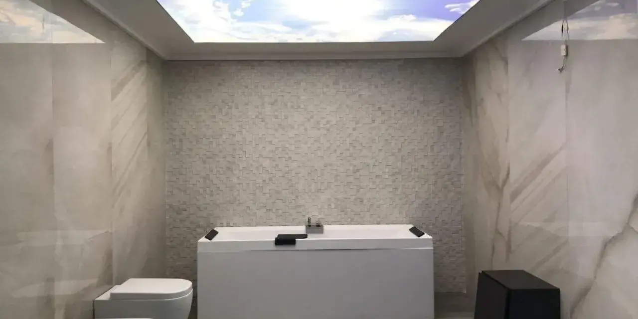 Bagno moderno con vasca, bidet e WC. Il soffitto in cartongesso riproduce un cielo azzurro con nuvole, creando un'atmosfera rilassante.