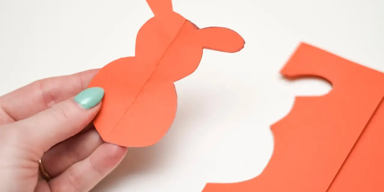 En hand håller en orange pappersfigur av en påskhare.