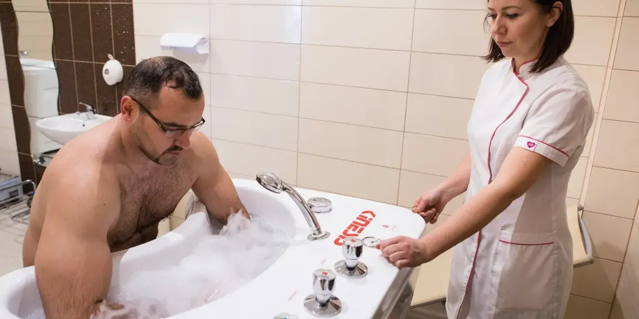 Mężczyzna w wannie z pianą, terapeuta przygotowuje masaż wirowy kończyn dolnych.