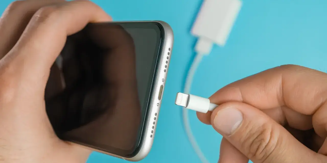 En hand håller en iPhone och en laddkabel. Var försiktig med vatten i ladduttaget på din iPhone.