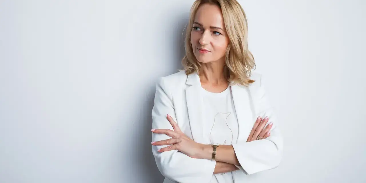Elegancka kobieta w białej marynarce, z rękami skrzyżowanymi na piersi. Idealne zdjęcie do CV, podkreślające profesjonalizm i pewność siebie.