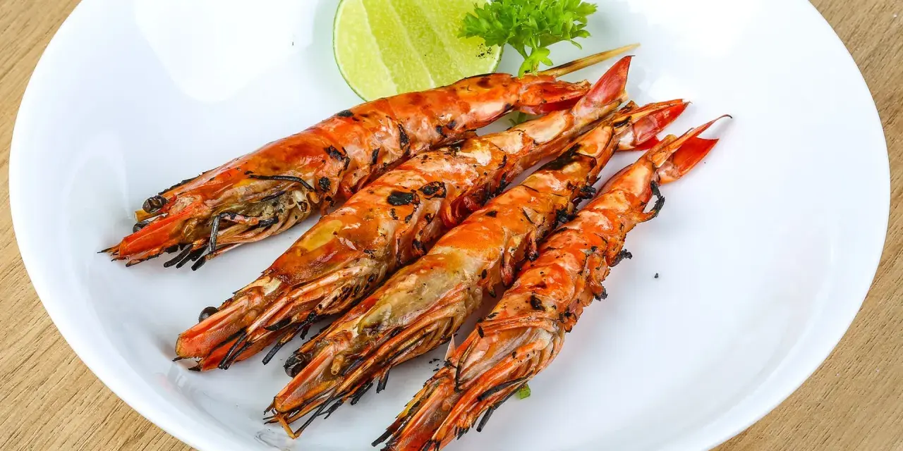 Cuatro langostinos a la plancha, dorados y jugosos, servidos en plato blanco con rodaja de limón y perejil.