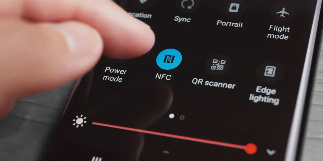 En finger pekar på NFC-ikonen på en mobilskärm. Snabbinställningar visas, inklusive "Power mode" och "QR scanner".