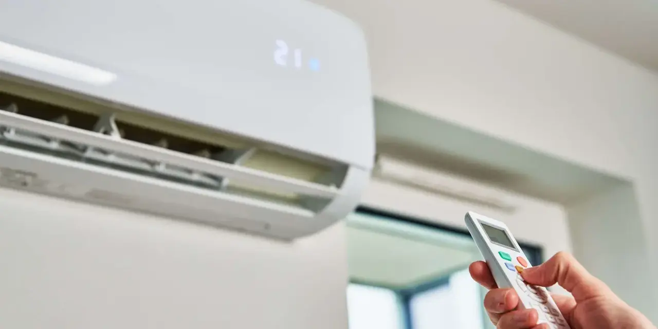 Mano operando el control remoto de un aire acondicionado, indicando la temperatura de 21 grados. Es hora del mantenimiento.